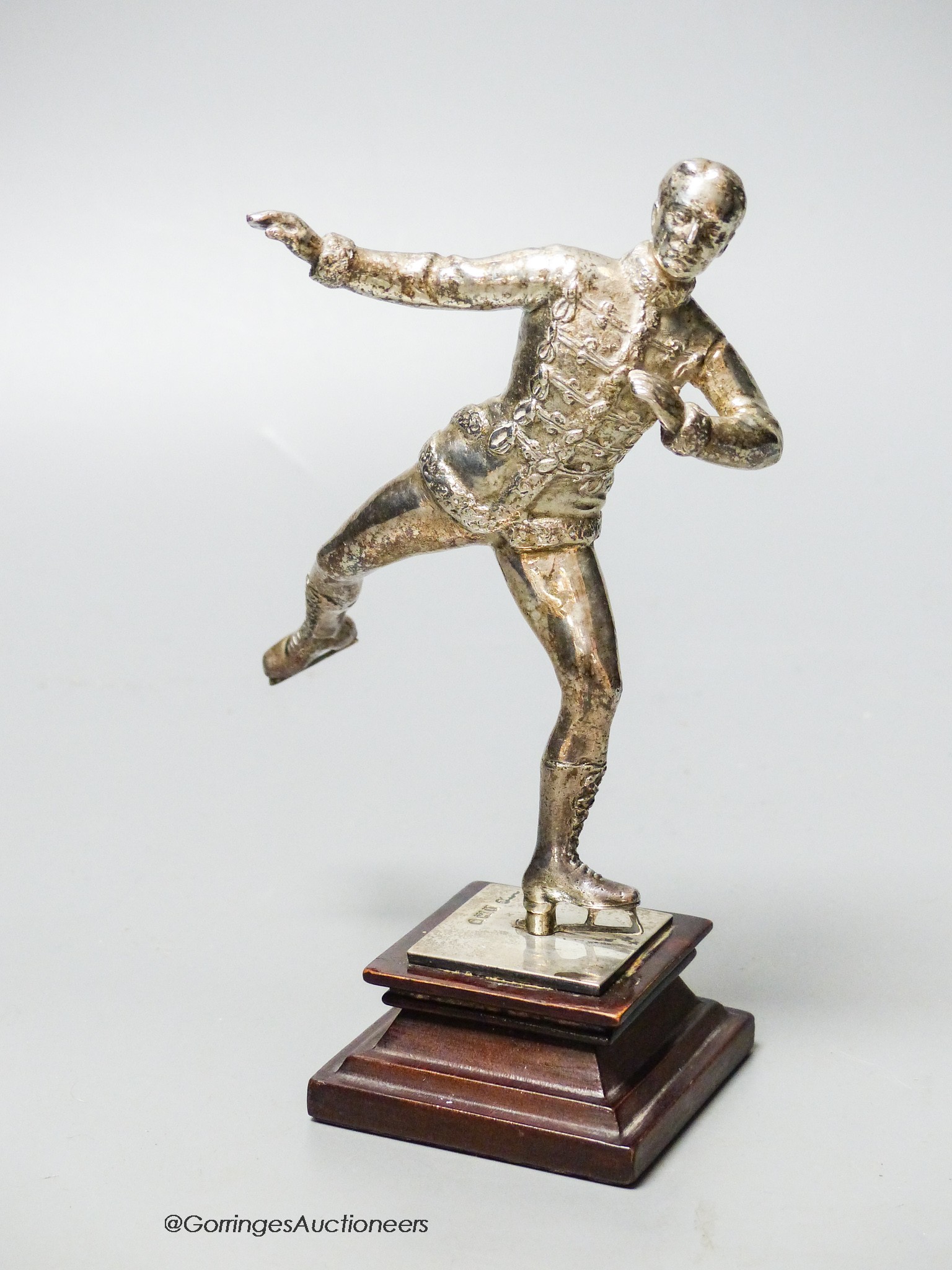 An Edwardian silver miniature model of an ice skater, Elkington & Co Ltd?, London, 1904, on a wooden plinth base, skater 12cm, gross weight 10oz.